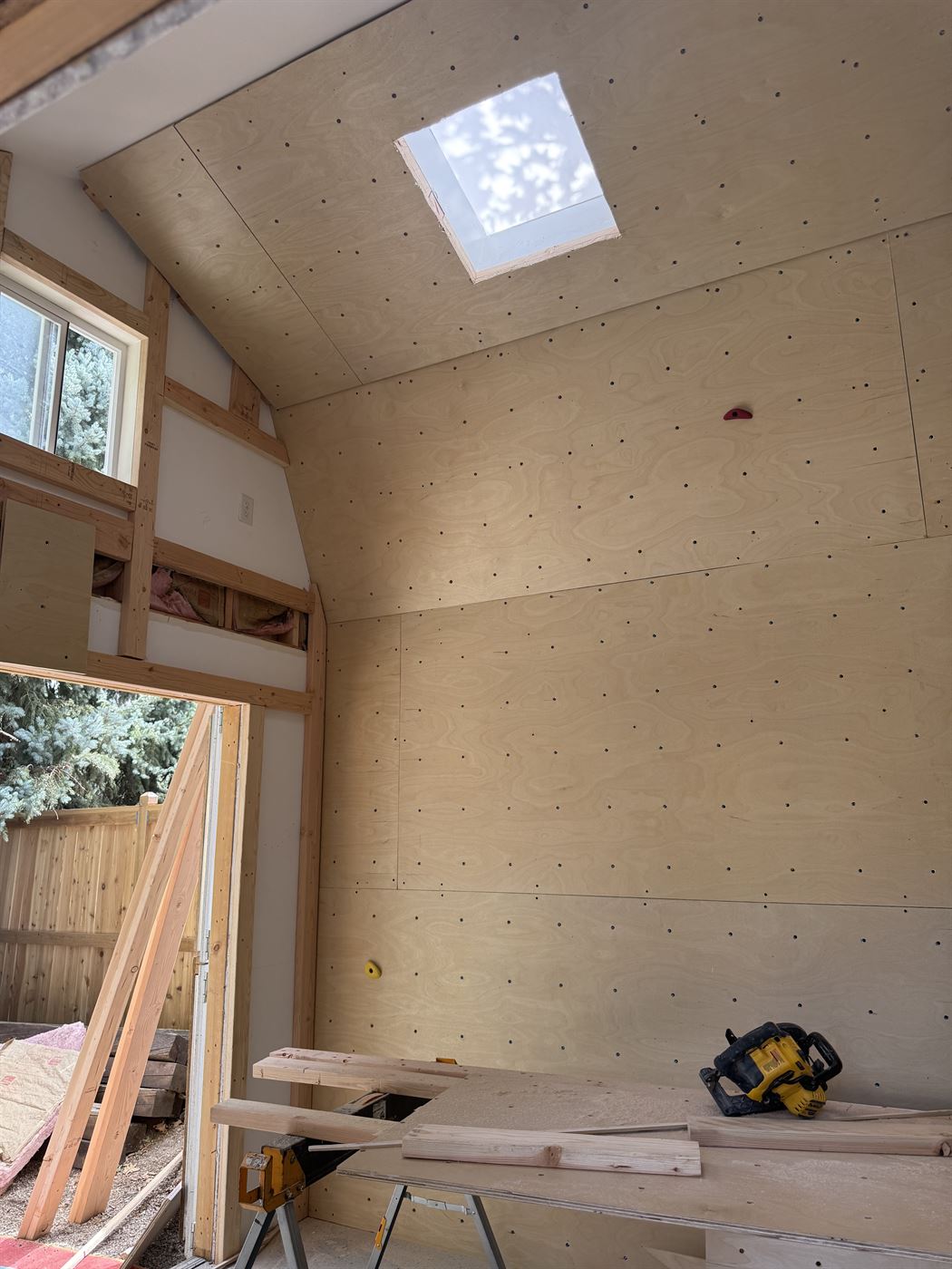 Climbing wall panels installed in a shed, showing plywood boards with T-nut holes on walls and angled ceiling