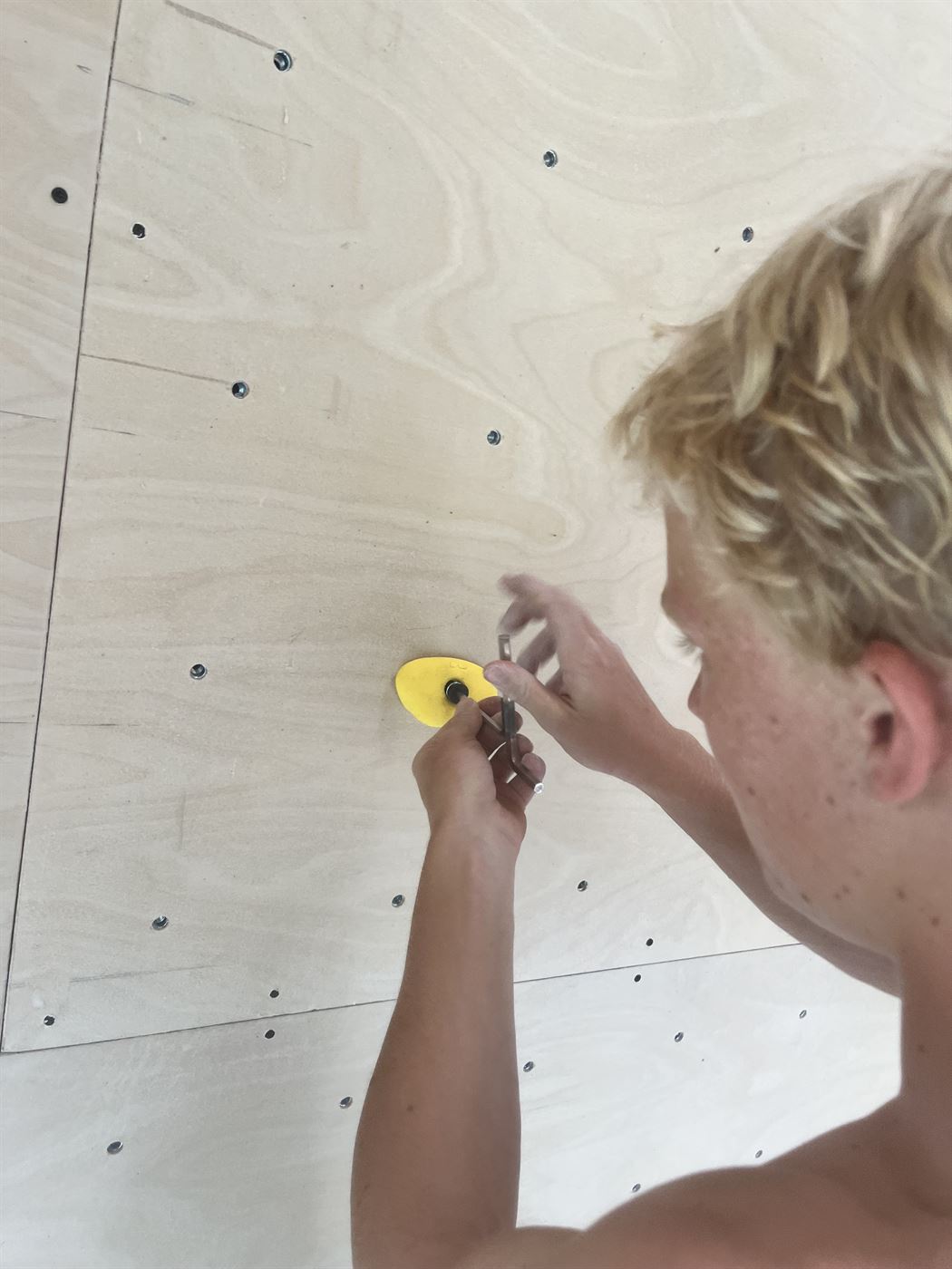 Person screwing a yellow climbing hold into a panel T-nut